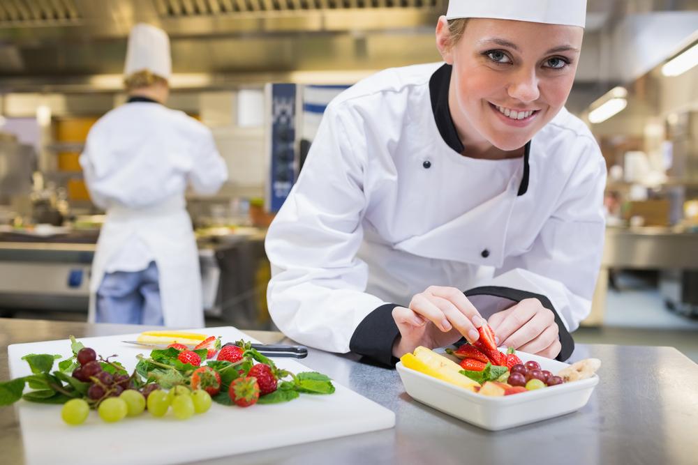 Smiling chef putting a strawberry in the fruit bowl in the kitchen